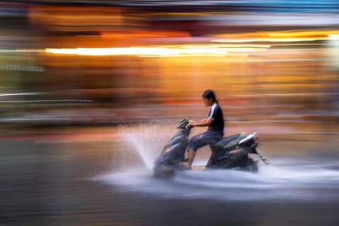 Young woman rides motor scooter at speed in rain along flooded De Tham Street Pham Ngu Lao district Ho Chi Minh City Vietnam
